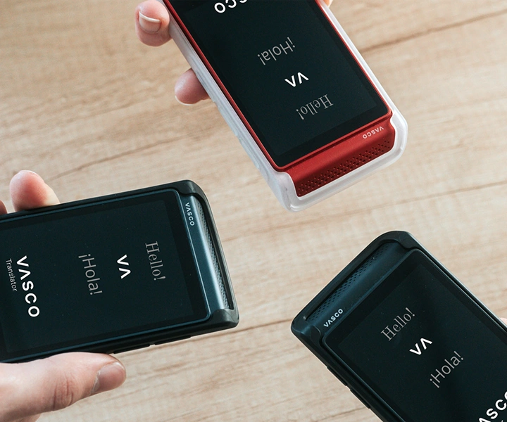Kolme henkilöä, joilla on Vasco Translator Q1 -laitteet, tuovat ne yhteen; laitteiden näytöillä näkyy aloitusnäyttö, jossa on Vasco-logo sekä sanat ”Hello!” ja ”¡Hola!”. Laitteet on varustettu silikonikoteloilla, joita on saatavana kolmessa värissä: Solid Black, Dark Caramel ja Milky White.