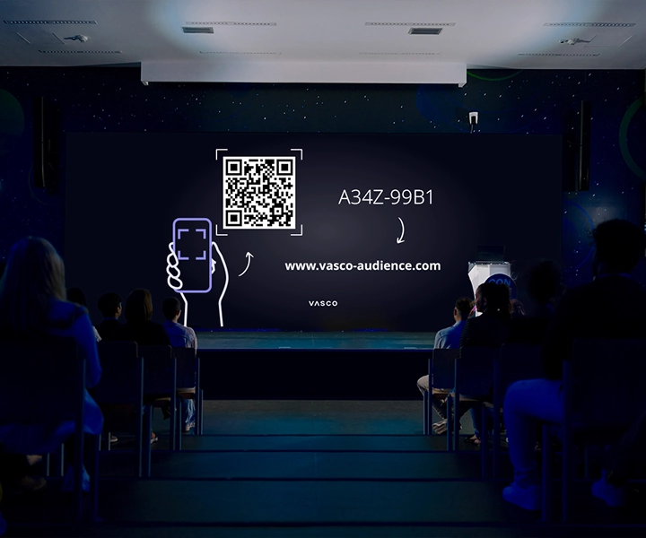 Suuri konferenssihuoneen näyttö näyttää ohjeet "Liity Vasco Audienceen", joissa osallistujille annetaan ohjeet istuntoon liittymisestä.